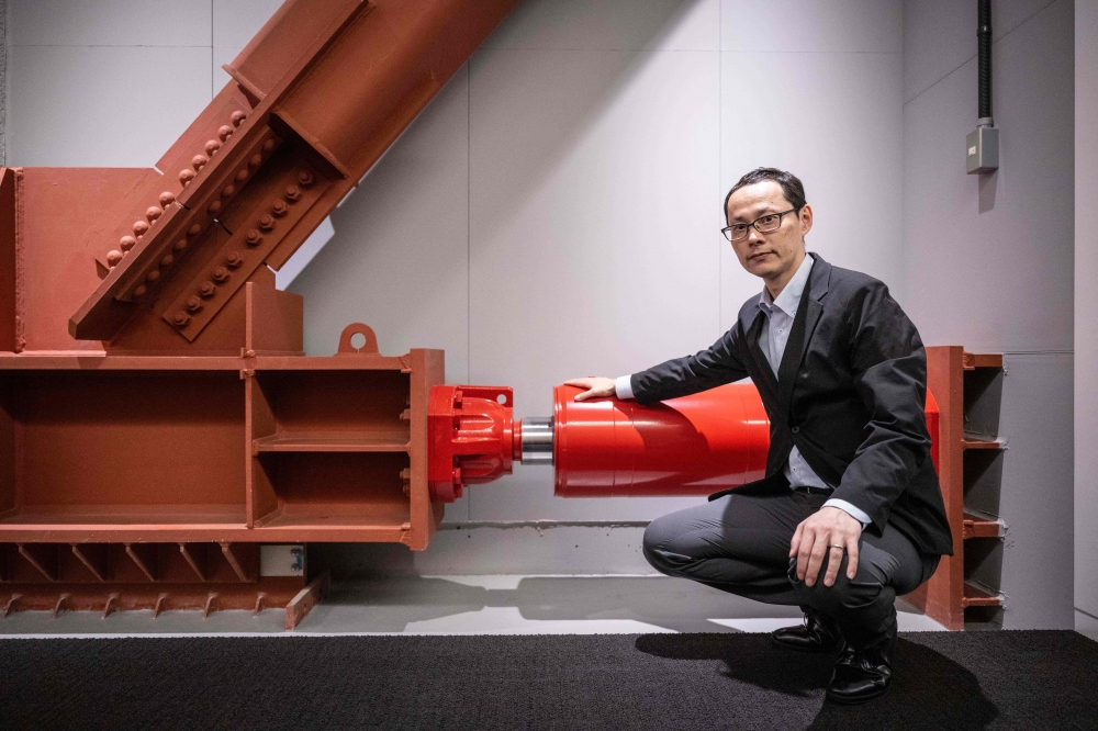 Kai Toyama, a structural engineering official at real estate giant Mori Building, posing for photographs with an oil damper at Toranomon Hills Business Tower in Tokyo. — eNM pic