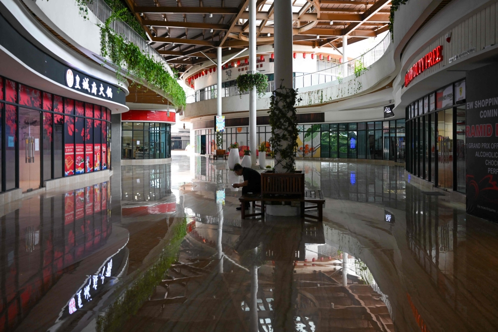 A man sits in the hallway in front of empty Forest City Outlet Mall, a development project launched under China's Belt and Road Initiative in Gelang Patah in Malaysia's Johor state on September 1, 2023. — eNM pic