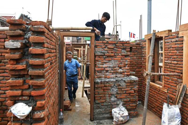 In this photograph taken on June 14, 2023, heritage conservationist and Nepal Vocational Academy founder Rabindra Puri (L) walks past a labourer working to reconstruct a temple in Bhaktapur on the outskirts of Kathmandu. — eNM pic