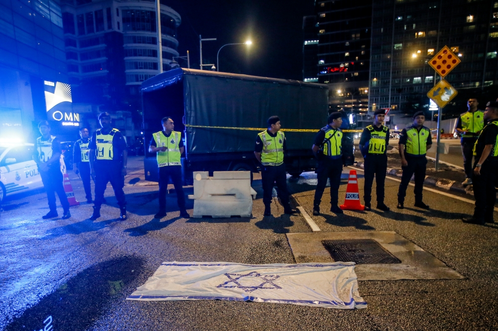 Police personnel guarding the US Embassy compound in front of an Israeli flag spread by protestors on the ground at Jalan Tun Razak in Kuala Lumpur, December 26, 2023. — Picture by Hari Anggara.