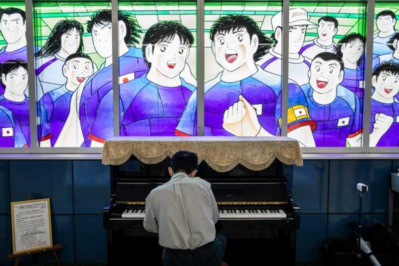 A train passenger plays piano next to stained glass artwork depicting the 