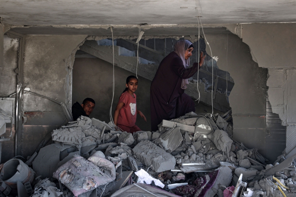 A Palestinian woman and children check the rubble of a building hit by overnight Israeli bombing in Rafah. — eNM pic