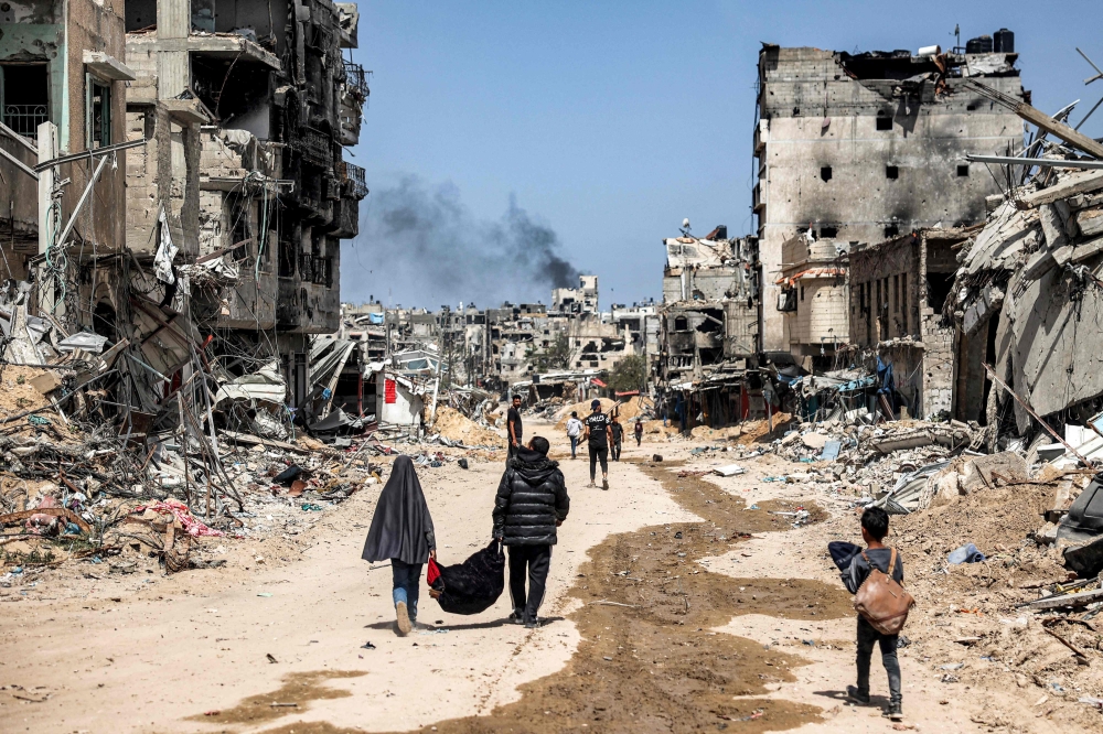 People walk with salvaged items past destroyed buildings in Khan Yunis in the southern Gaza Strip on April 22, 2024 amid the ongoing conflict in the Palestinian territory between Israel and Hamas. — eNM pic