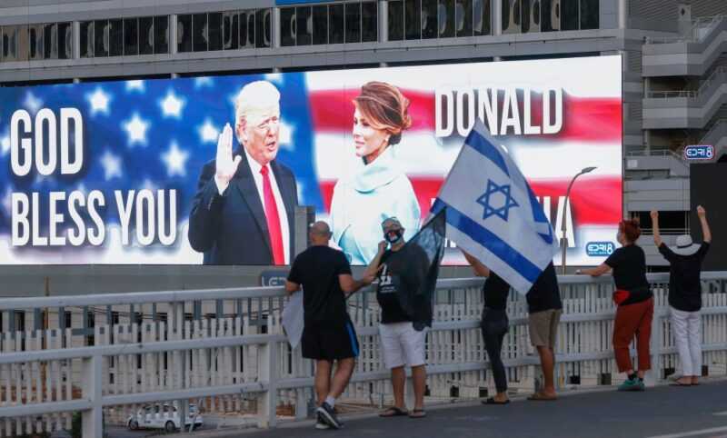 File photo of people lifting a national flag on an overpass facing a large billboard depicting the US President Donald Trump and his wife Melania on a building in the Israeli coastal city of Tel Aviv, on October 3, 2020. — eNM pic